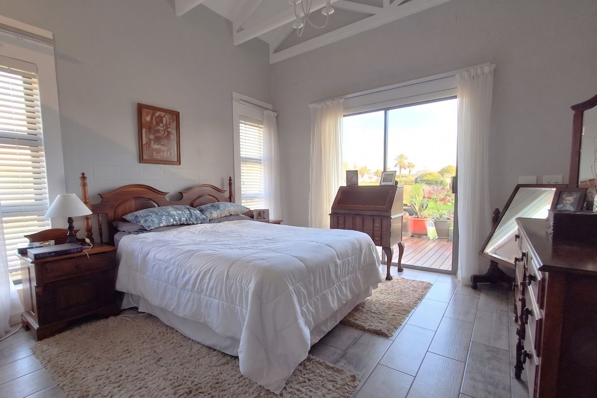 Spacious bedroom featuring vaulted ceilings with exposed rafters, tiled flooring, and a sliding glass door providing direct access to the outdoor patio area.