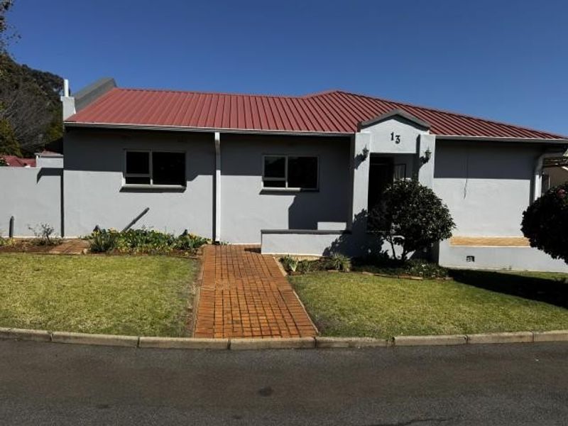 Front elevation of a single-story house featuring a red metal roof, grey exterior walls, and a brick-paved entrance walkway.