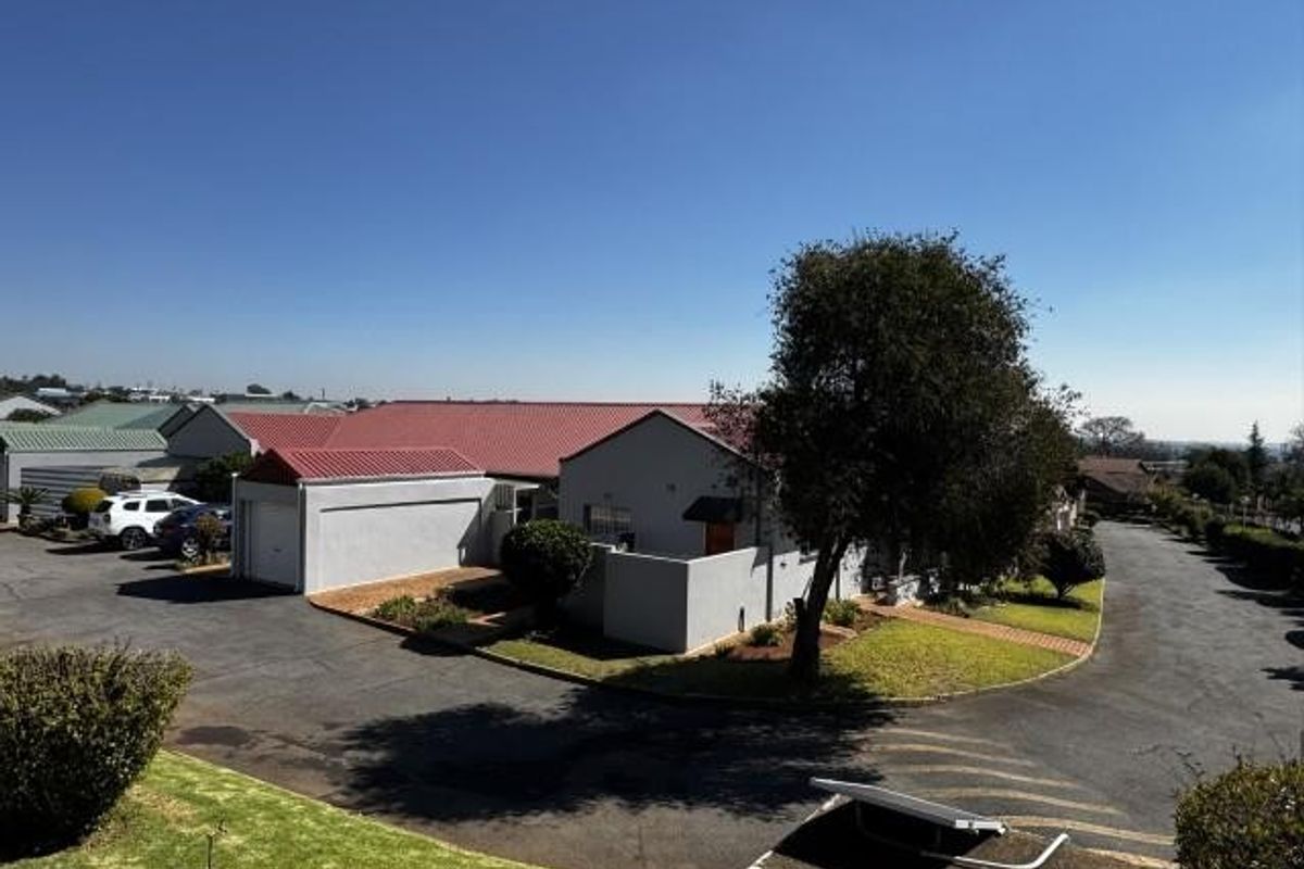 Aerial view of a residential property featuring a metal roof, attached garage, and paved driveway within a landscaped estate setting.