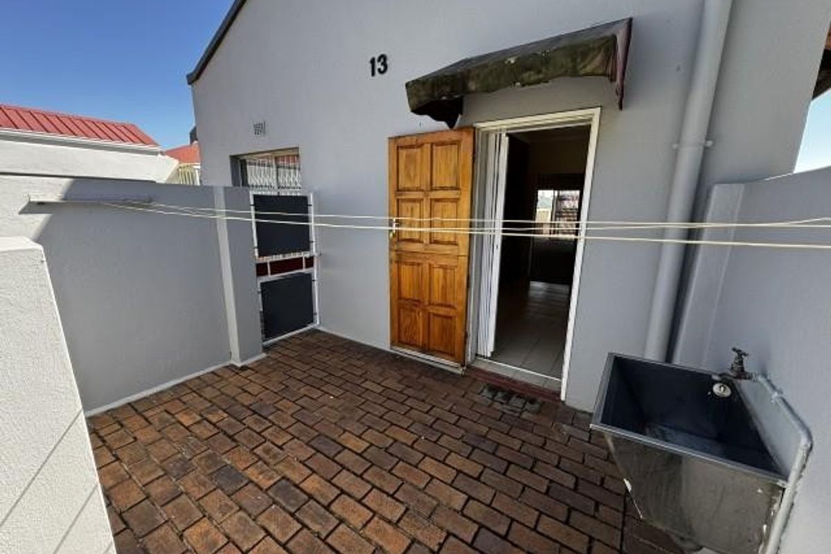 A paved rear courtyard area featuring a laundry sink, timber entrance door, and a protective awning over the doorway.