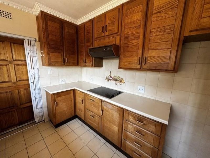 A functional kitchen featuring traditional wooden cabinetry, laminate countertops, an integrated electric hob with extractor fan, and tiled flooring.