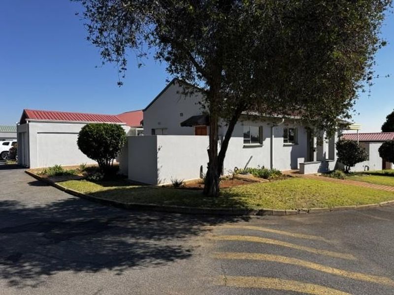 Front exterior view of the house featuring a metal roof, concrete driveway, and a detached garage with surrounding garden space.