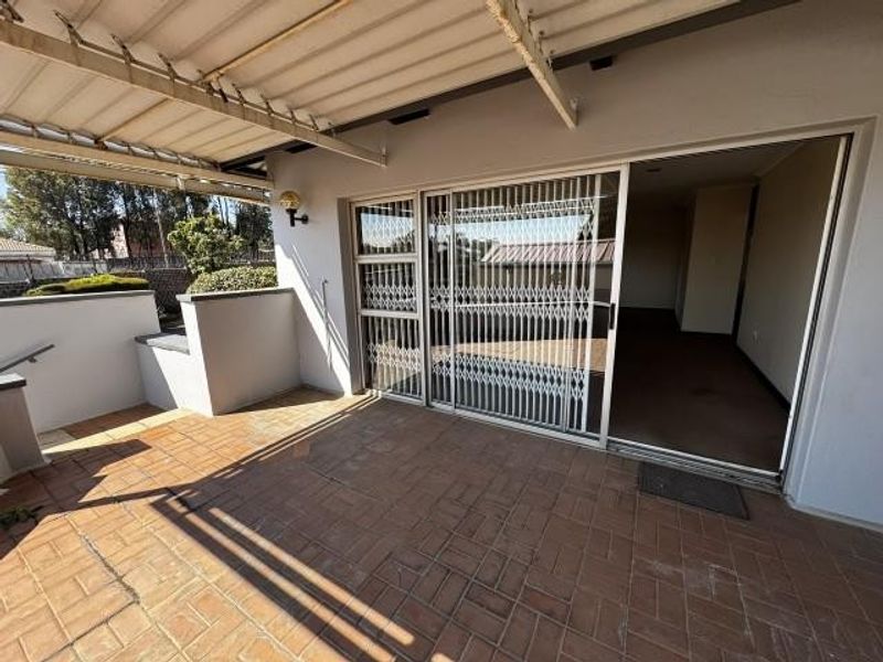 A covered outdoor patio area featuring brick paving, a sliding glass door with security gate, and direct access to the interior living space.