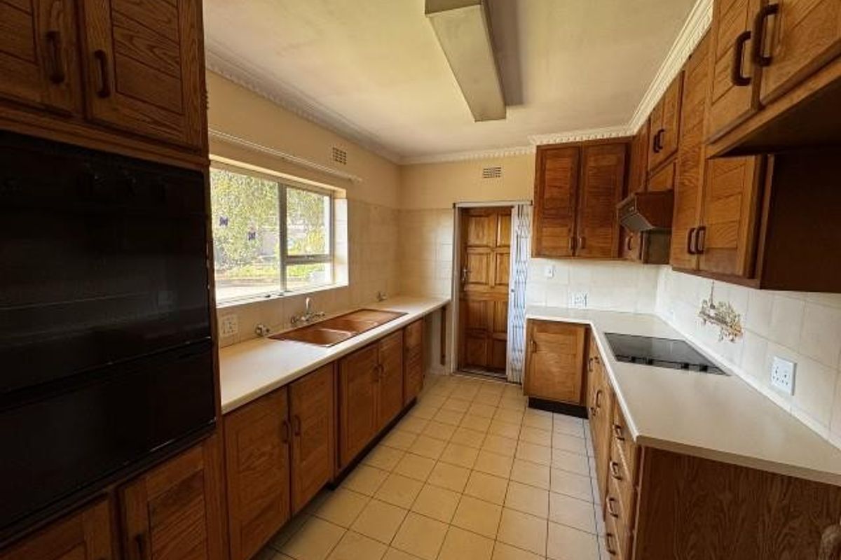 A functional kitchen featuring extensive wooden cabinetry, built-in oven, electric hob, double sink, and tiled flooring, offering a classic layout ready for modernization.