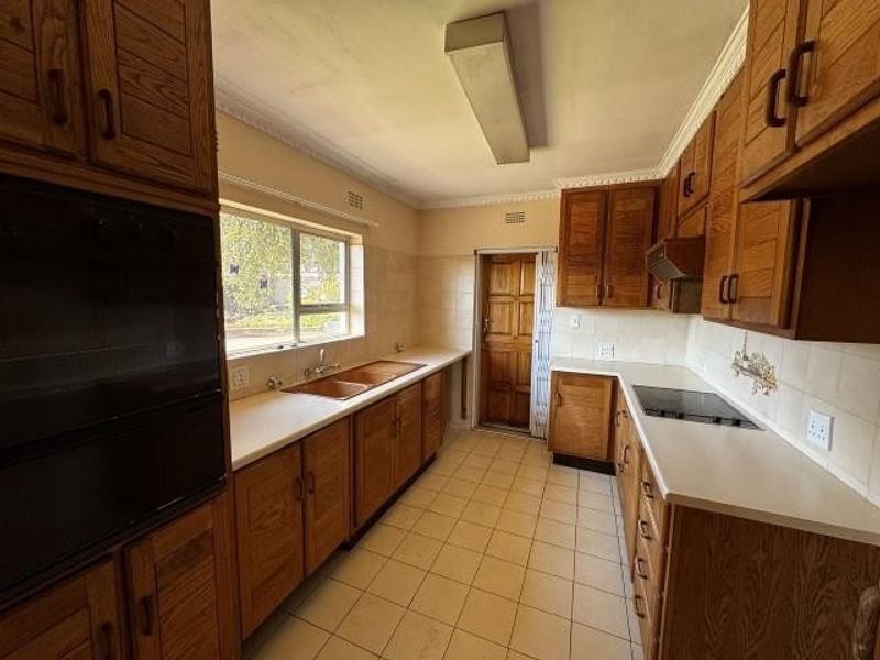 A functional kitchen featuring extensive wooden cabinetry, built-in oven, electric hob, double sink, and tiled flooring, offering a classic layout ready for modernization.