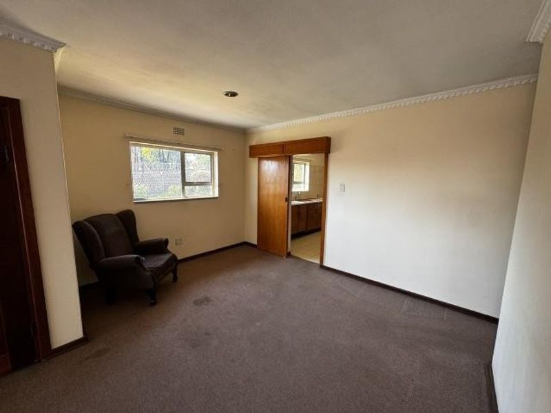 A spacious, neutrally painted living area featuring carpet flooring, crown molding, and a sliding wooden door leading to the kitchen area.