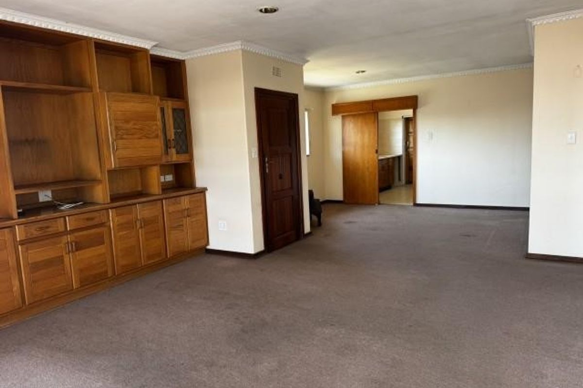 Spacious living area featuring extensive built-in wooden cabinetry, crown molding, and neutral wall finishes, offering a versatile layout for renovation.
