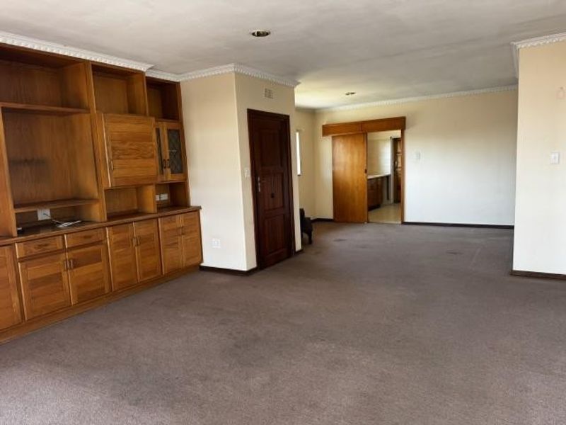 Spacious living area featuring extensive built-in wooden cabinetry, crown molding, and neutral wall finishes, offering a versatile layout for renovation.