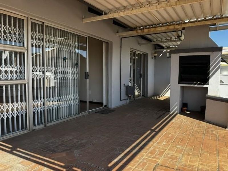A covered patio area featuring a built-in braai, tiled flooring, and sliding door access to the interior living space.