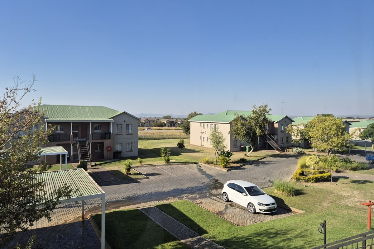 An elevated view of an apartment complex featuring multiple buildings with metal roofs, paved parking areas, and well-maintained communal garden spaces.