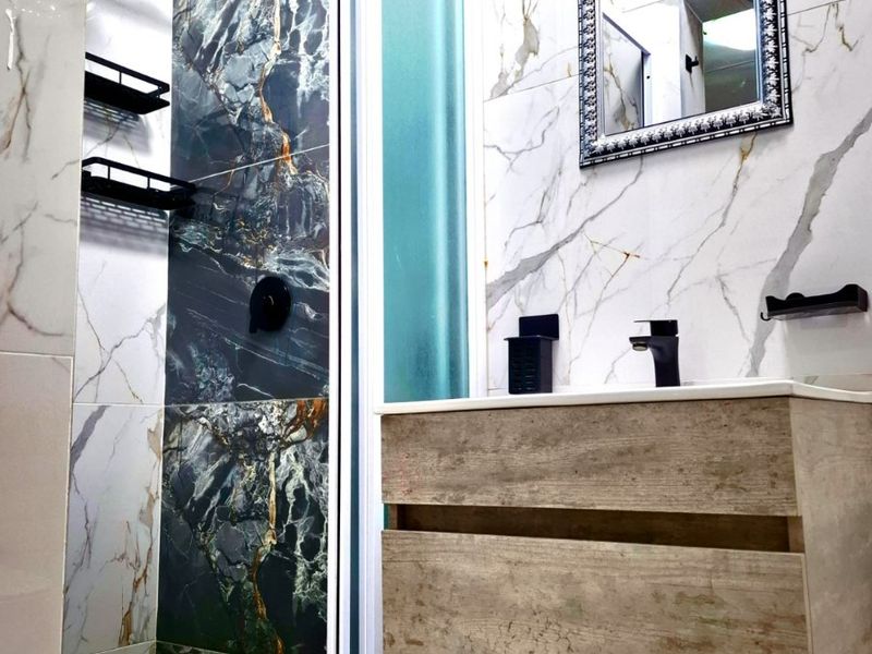 Modern bathroom featuring a walk-in shower with rain shower head, marble-effect tiling, and a contemporary wall-mounted vanity with a black faucet.