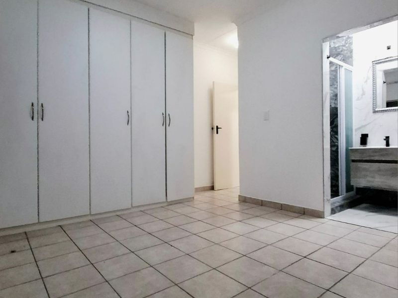 A spacious, empty bedroom featuring built-in cupboards, tiled flooring, and direct access to an en-suite bathroom.