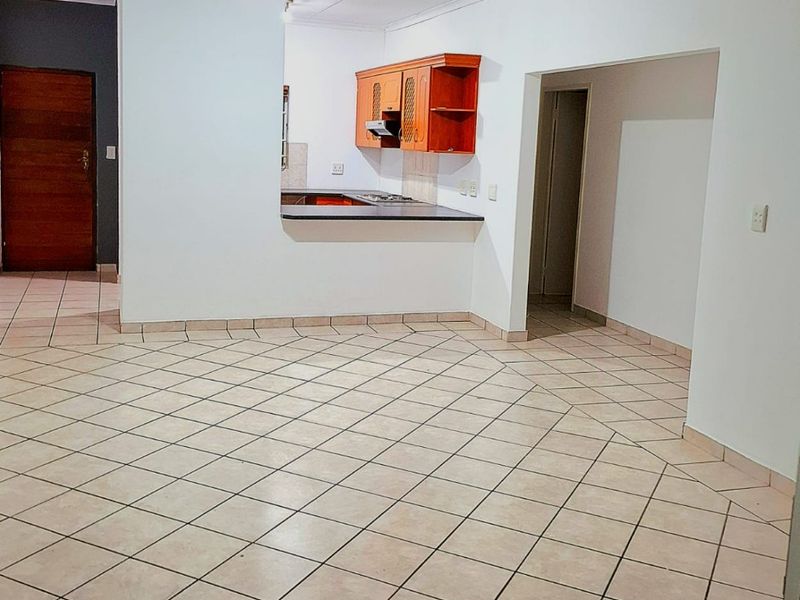 An open-plan living area featuring ceramic tile flooring and a functional kitchen with built-in cabinetry, hob, and extractor fan.