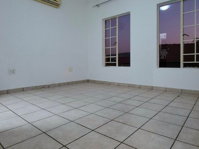 An empty bedroom featuring neutral ceramic floor tiles, a wall-mounted air conditioning unit, and large windows with grid detailing.