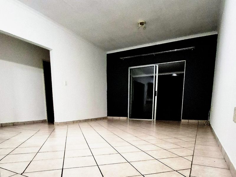 An empty living room featuring tiled flooring and a sliding glass door leading to an outdoor area.