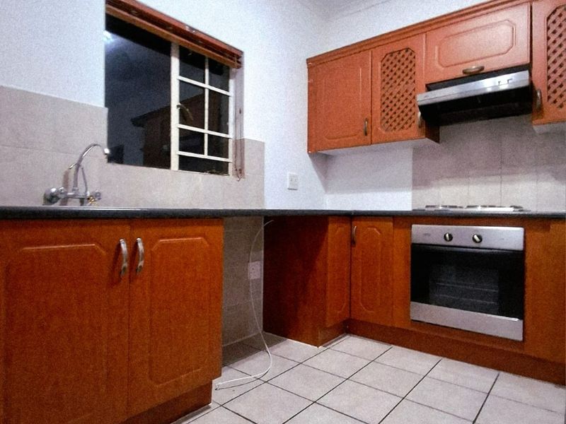 A functional kitchen featuring wooden cabinetry, built-in oven, gas hob, extractor fan, and tiled flooring with a neutral backsplash.