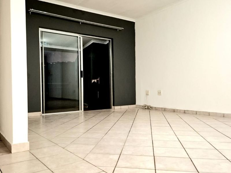 An empty living room featuring neutral ceramic floor tiles, a dark accent wall, and a sliding glass door leading to an outdoor area.