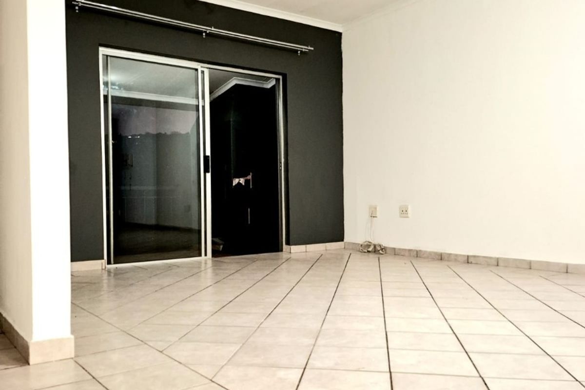 An empty living room featuring neutral ceramic floor tiles, a dark accent wall, and a sliding glass door leading to an outdoor area.