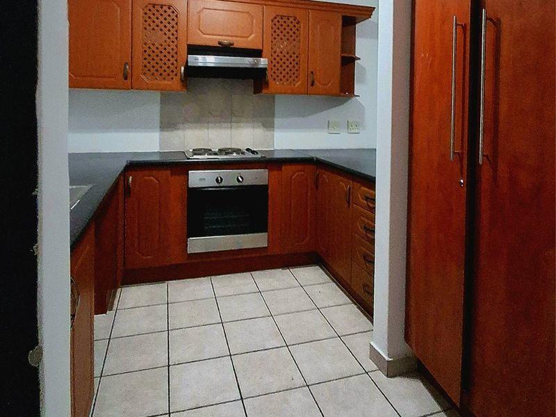 A functional kitchen featuring wooden cabinetry, stone countertops, a gas hob, built-in oven, and tiled flooring, offering a classic layout with ample storage space.