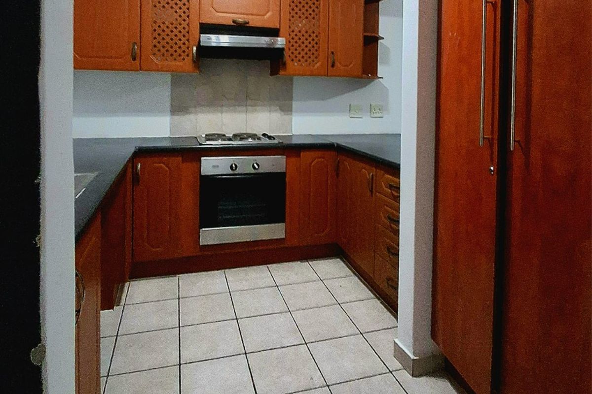 A functional kitchen featuring wooden cabinetry, stone countertops, a gas hob, built-in oven, and tiled flooring, offering a classic layout with ample storage space.