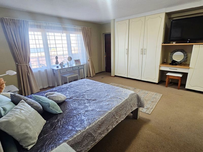 Spacious bedroom featuring extensive built-in cabinetry, a dedicated vanity area, and large windows with security bars.