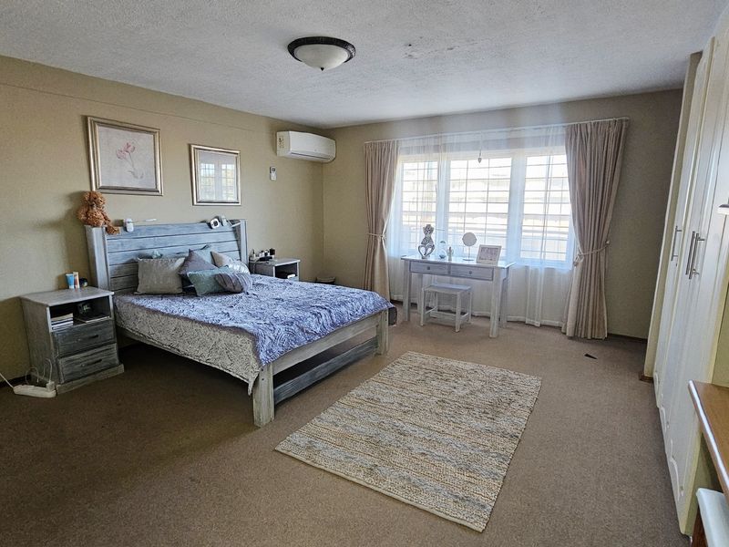 Spacious bedroom featuring built-in cupboards, carpeted flooring, and a wall-mounted air conditioning unit, offering a comfortable and functional living space.