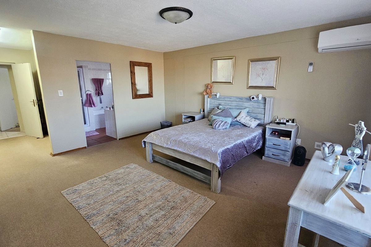 Spacious bedroom featuring neutral wall tones, carpeted flooring, an integrated air conditioning unit, and direct access to an en-suite bathroom.