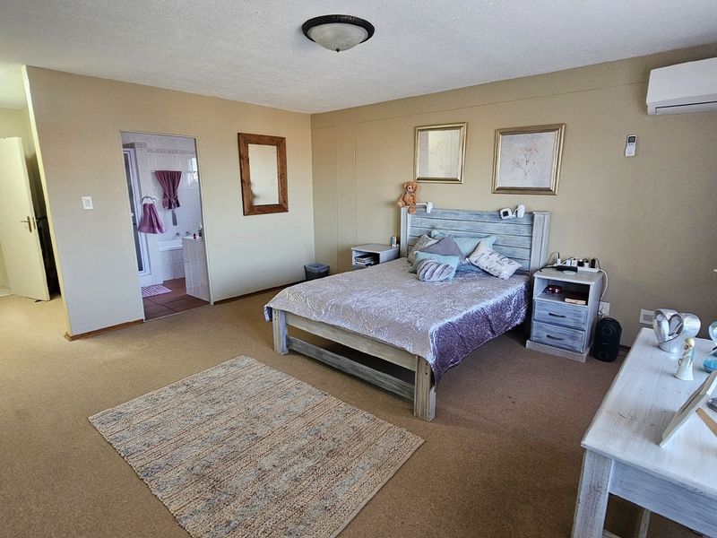 Spacious bedroom featuring neutral wall tones, carpeted flooring, an integrated air conditioning unit, and direct access to an en-suite bathroom.