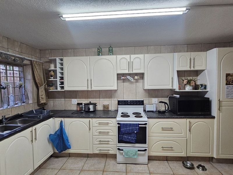 A functional kitchen featuring cream-colored cabinetry, dark laminate countertops, a tiled backsplash, and a freestanding stove with ample storage space.