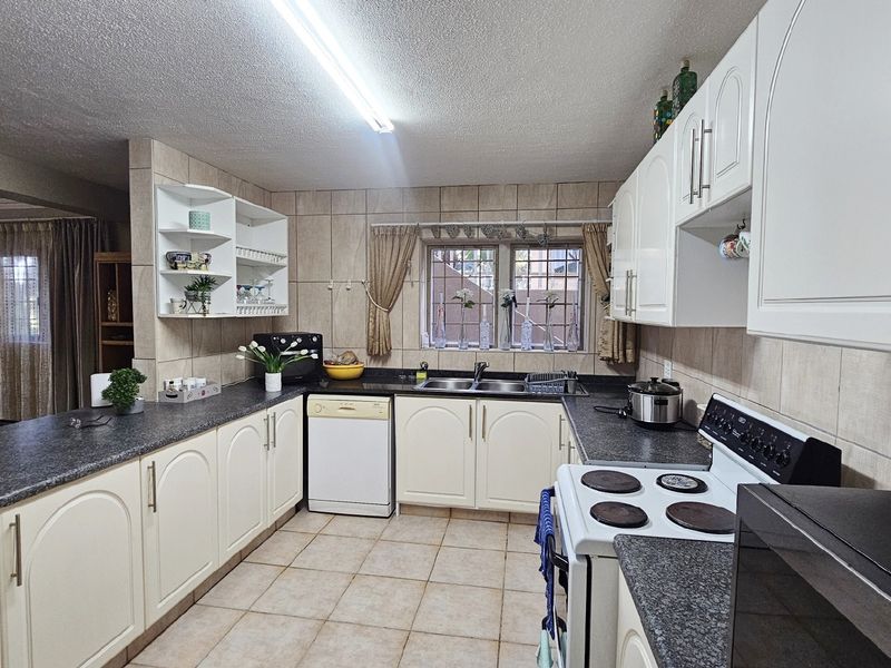 A functional kitchen featuring white cabinetry, granite countertops, tiled backsplash, and a double basin sink, with direct access to the adjacent living area.