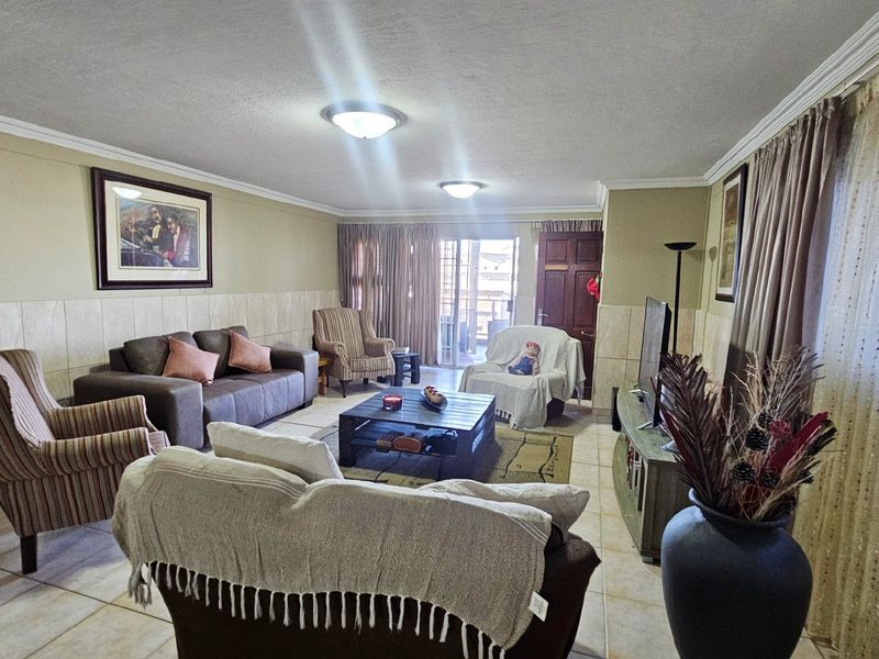 A spacious living room featuring tiled flooring, partial wall tiling, and a sliding glass door providing access to the outdoor area.