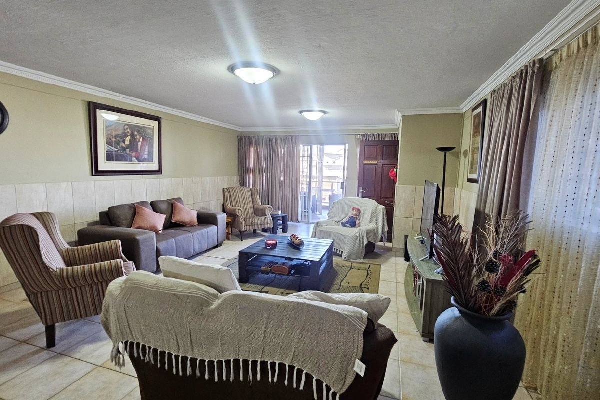 A spacious living room featuring tiled flooring, partial wall tiling, and a sliding glass door providing access to the outdoor area.