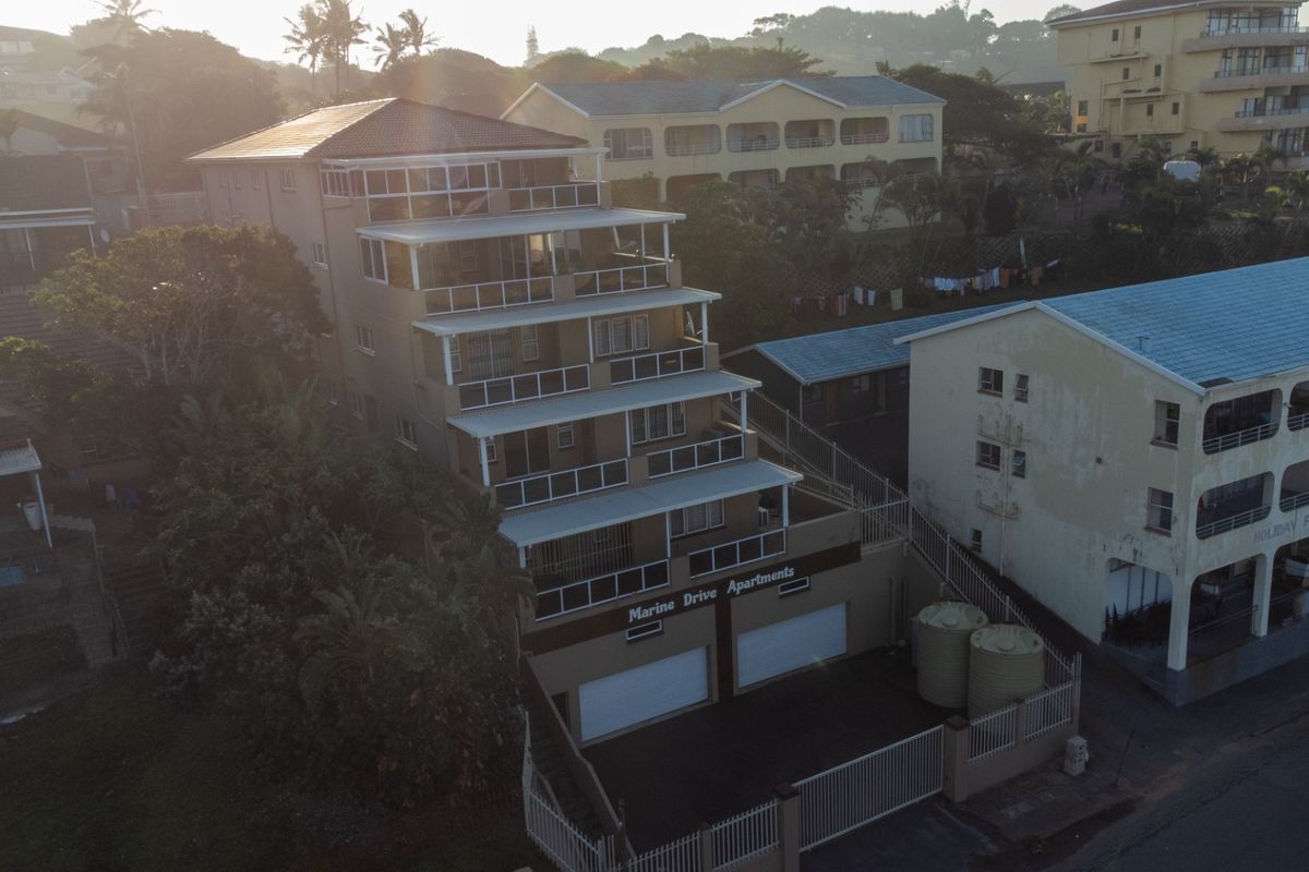 Aerial view of a multi-story apartment complex featuring tiered balconies, ground-level garage access, and exterior water storage tanks.