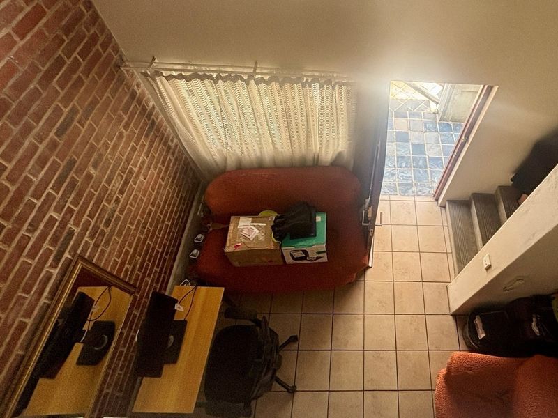 A high-angle view of a living area featuring an exposed brick wall, tiled flooring, and direct access to an outdoor patio area.