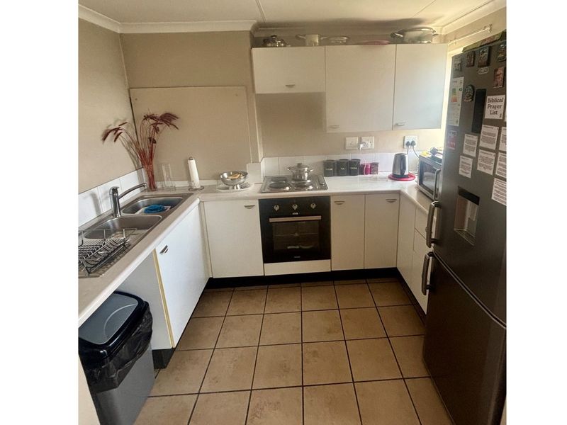 A functional kitchen featuring white cabinetry, built-in oven, gas hob, stainless steel sink, and tiled flooring.