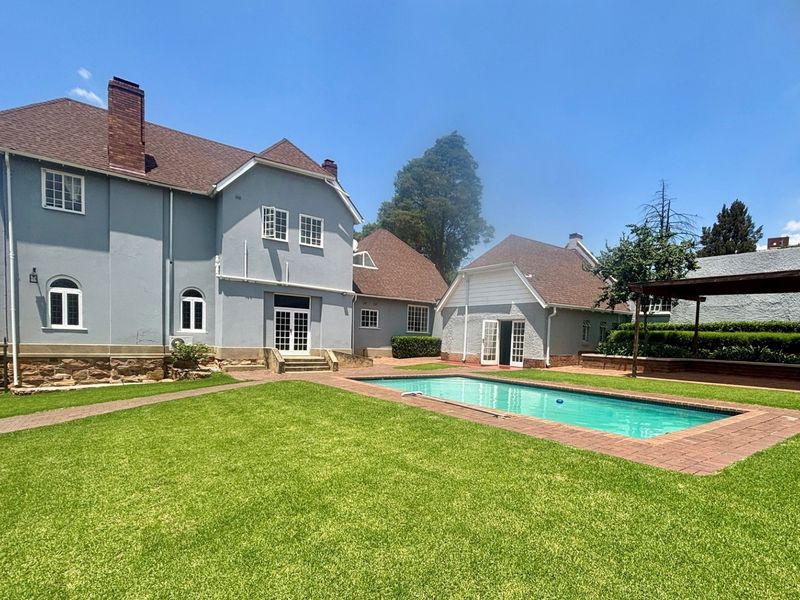 Spacious rear garden featuring a well-maintained swimming pool, brick paving, and a pergola, set against the backdrop of a charming multi-story townhouse.