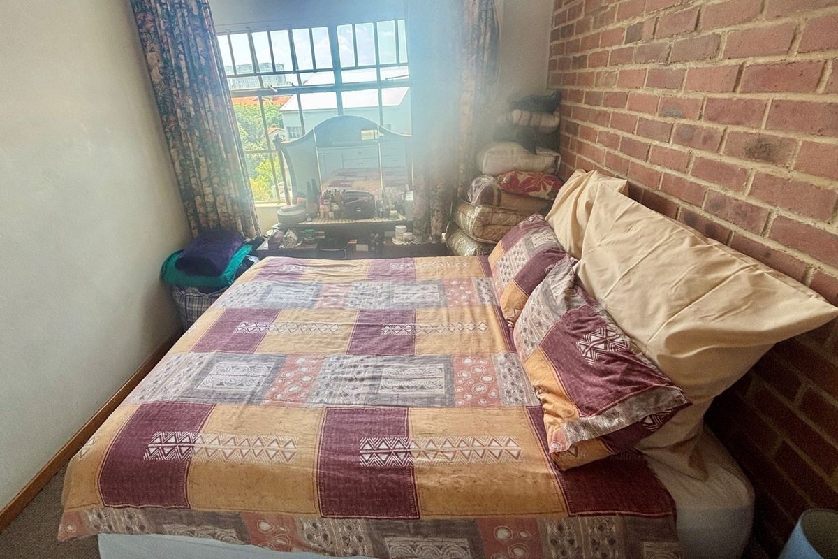 A bedroom featuring an exposed brick feature wall and a window with security bars, providing natural light.