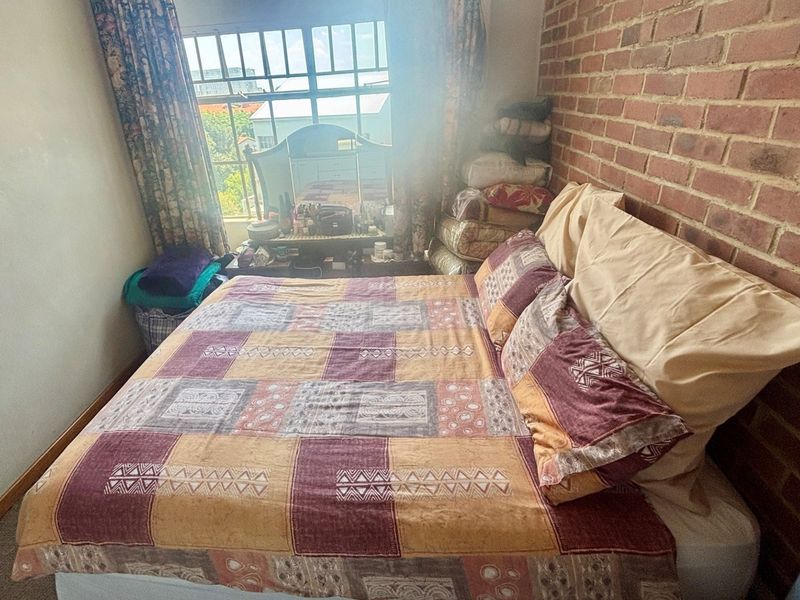 A bedroom featuring an exposed brick feature wall and a window with security bars, providing natural light.