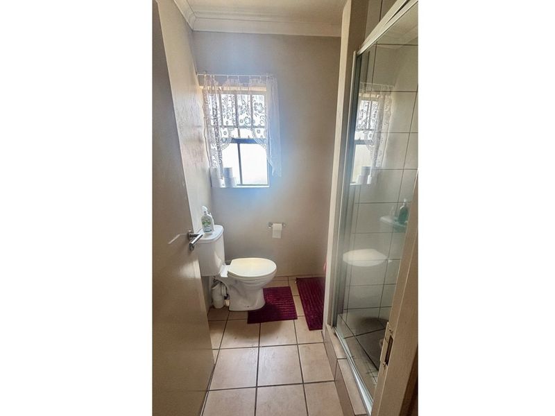A functional bathroom featuring a tiled floor, a standard toilet, and a glass-enclosed shower unit.