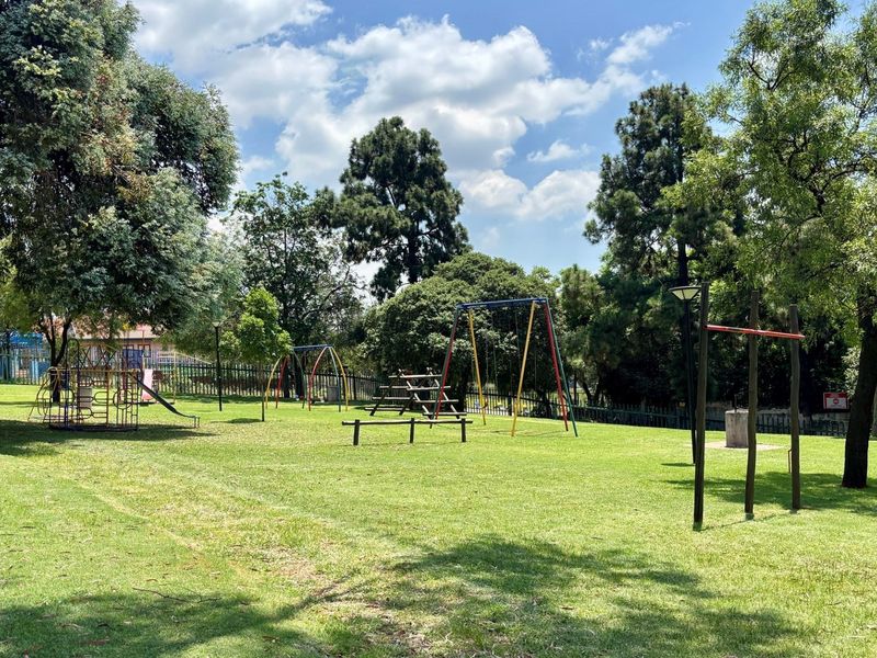A well-maintained communal garden area featuring established trees, lawn space, and playground equipment for residents.