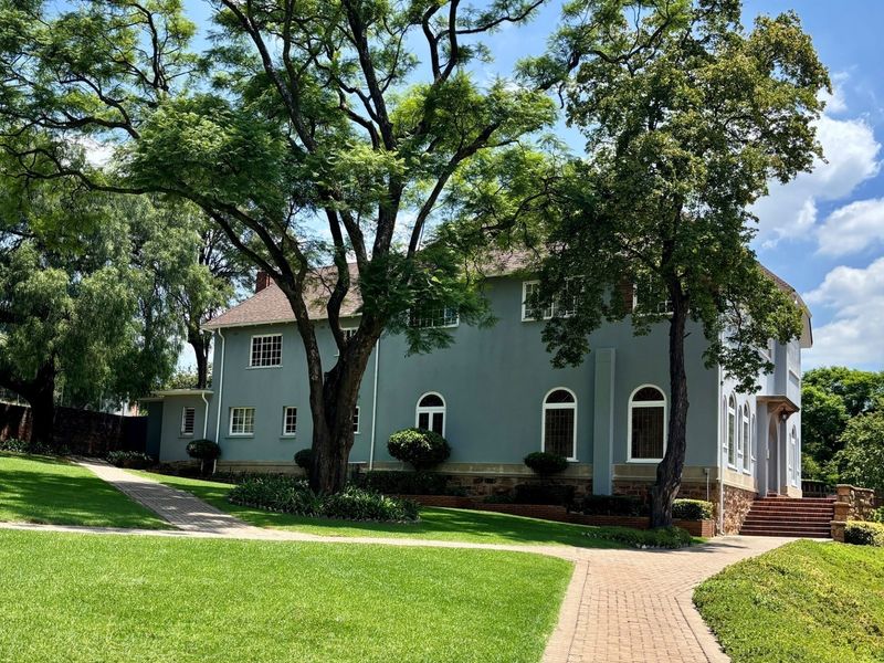 A well-maintained rear exterior view of the townhouse featuring a landscaped garden, mature trees, paved walkways, and classic arched window detailing.