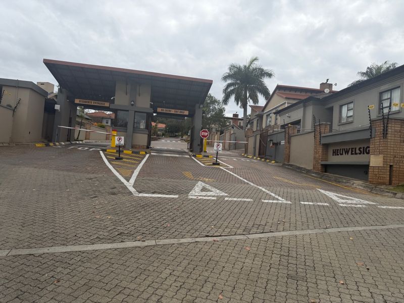The main entrance to the residential estate featuring a secure gatehouse, boom gates, and paved driveway access.