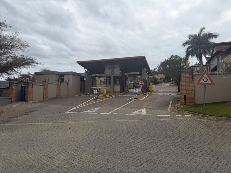 The entrance to the residential estate features a secure gatehouse, boom gates, and paved driveway access with perimeter walling and electric fencing.