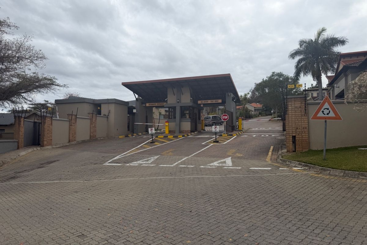The entrance to the residential estate features a secure gatehouse, boom gates, and paved driveway access with perimeter walling and electric fencing.
