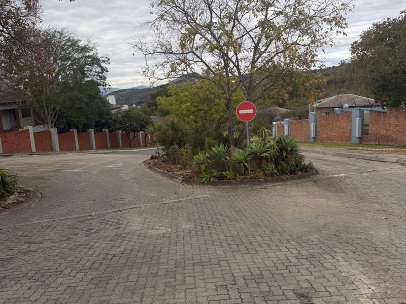 A view of the paved residential street and access road featuring established brick boundary walls and a landscaped traffic island.