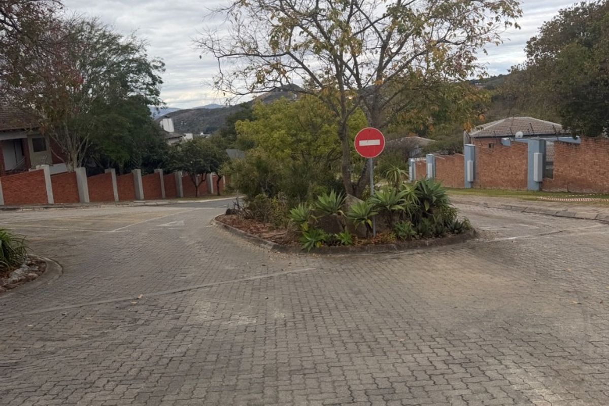 A view of the paved residential street and access road featuring established brick boundary walls and a landscaped traffic island.
