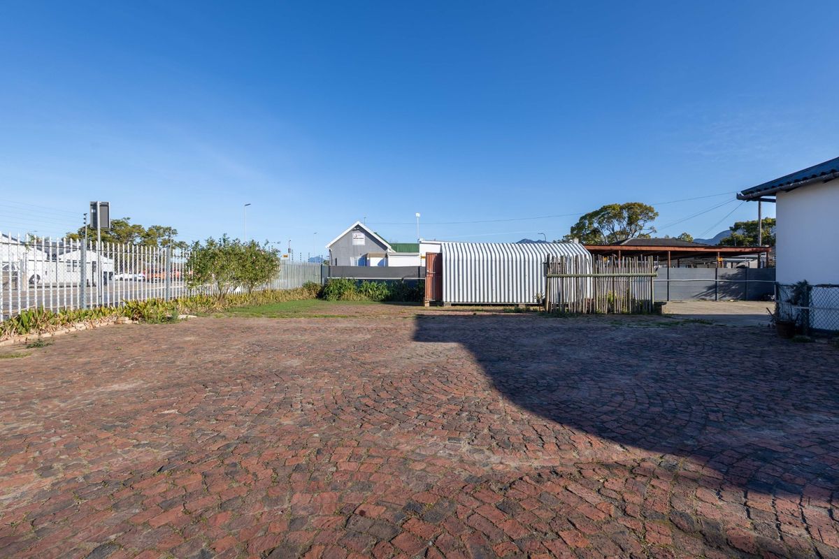 A spacious rear exterior area featuring cobblestone paving, metal perimeter fencing, and a corrugated metal storage structure.
