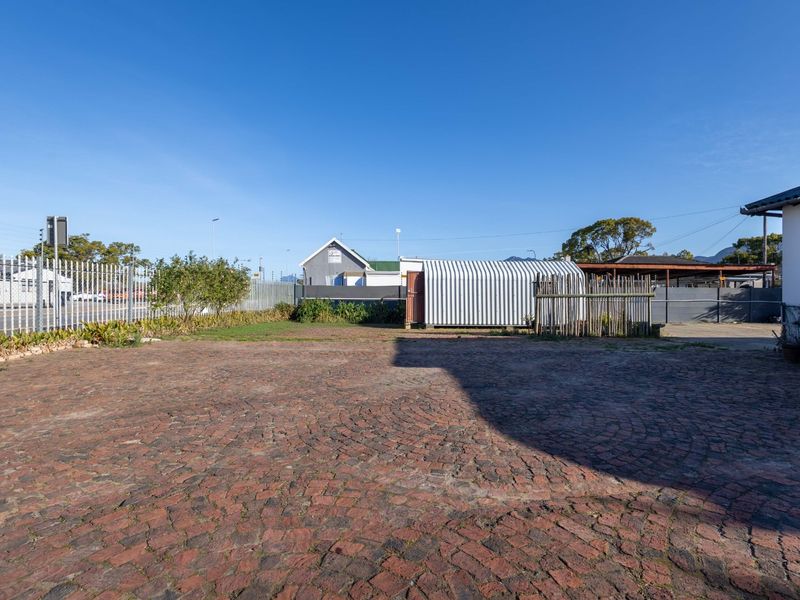 A spacious rear exterior area featuring cobblestone paving, metal perimeter fencing, and a corrugated metal storage structure.