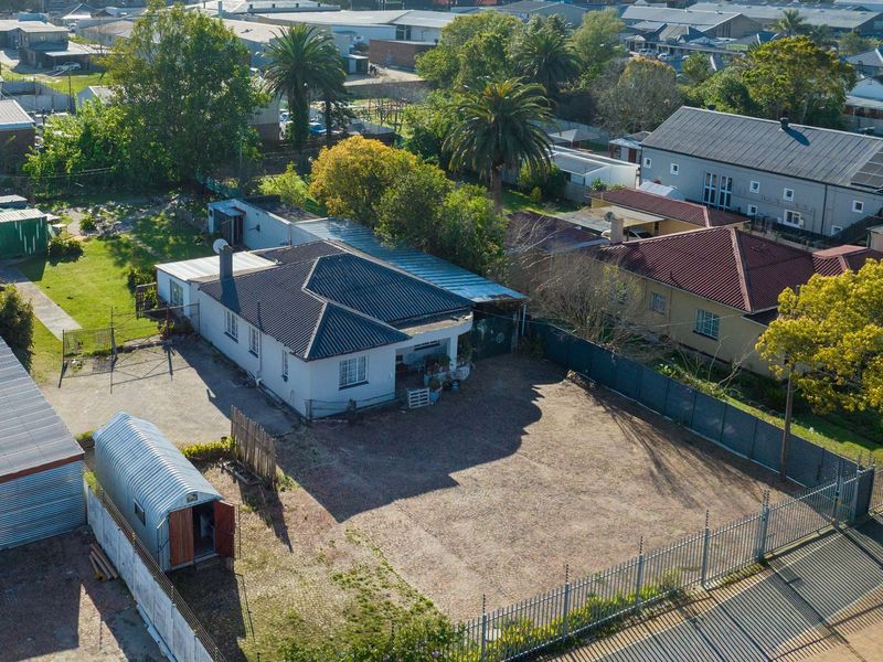 Aerial view of a commercial property featuring a main building with a metal roof, paved driveway, and secure perimeter fencing with electric security wires.