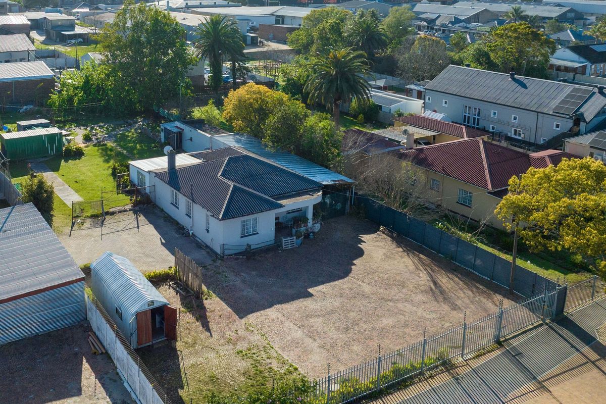 Aerial view of a commercial property featuring a main building with a metal roof, paved driveway, and secure perimeter fencing with electric security wires.